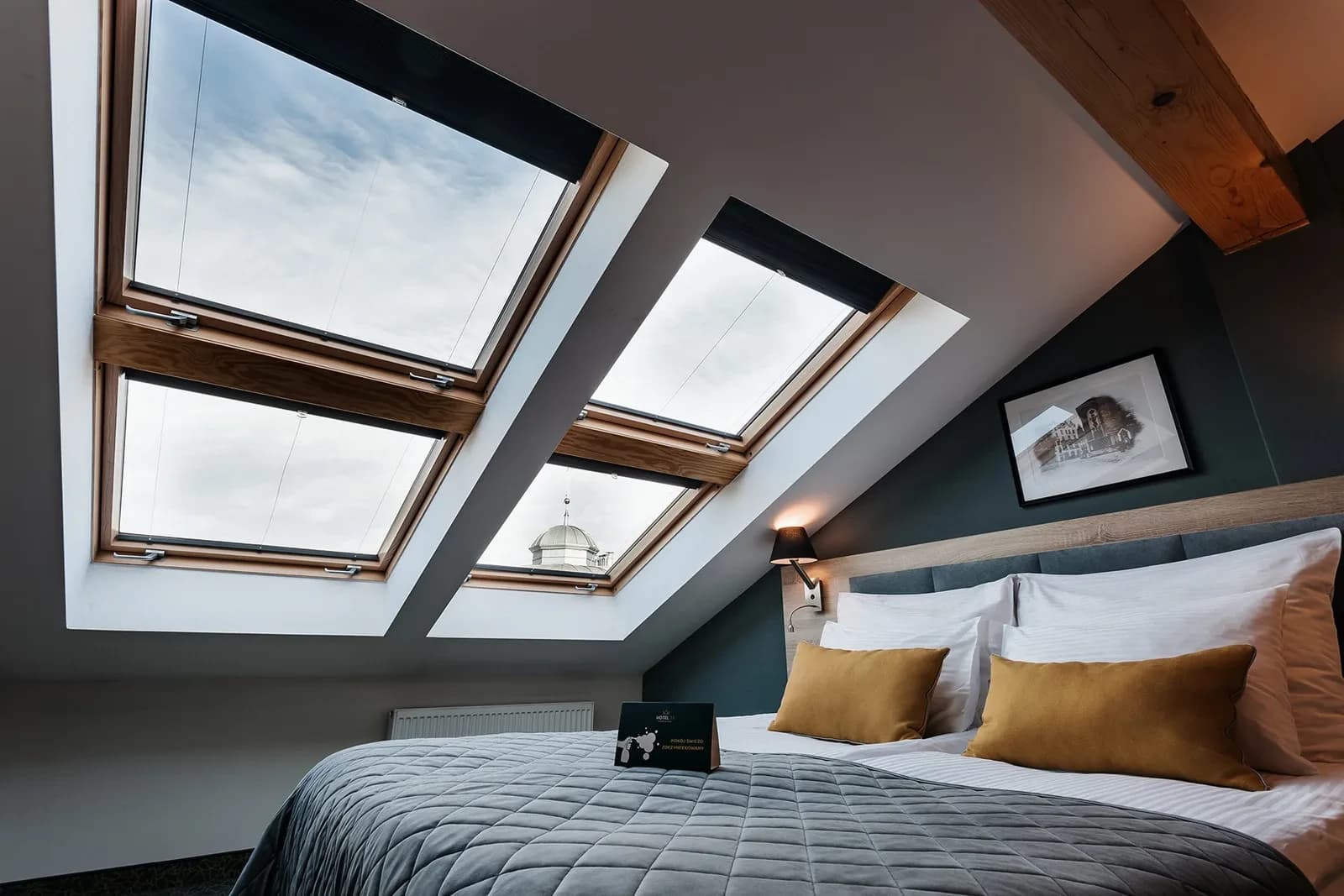Low-angle bed view beneath angled skylights, gray quilt, white linens and mustard pillows.